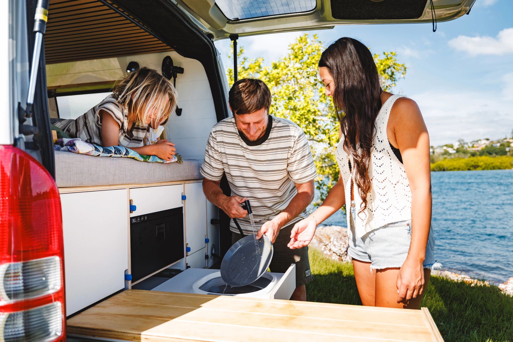 Family camping by lakeside preparing breakfast in camper van